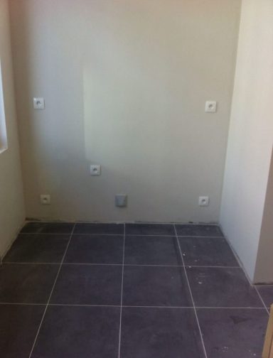 Mur non fini avec prises électriques et sol carrelé.