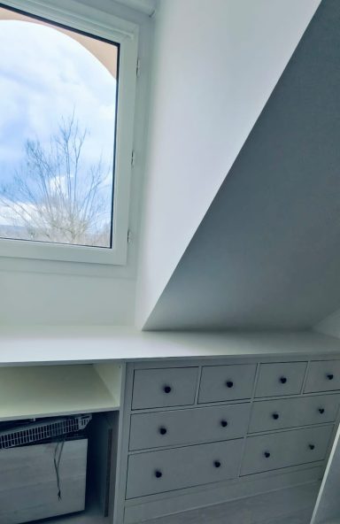 Fenêtre avec vue sur un ciel nuageux, bureau avec tiroirs en dessous.