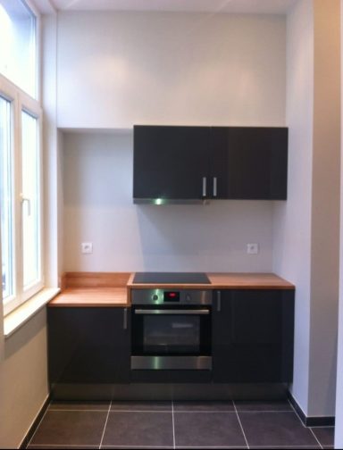 Cuisine moderne avec plans de travail en bois, four et placards noirs.
