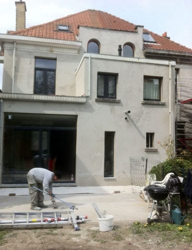 Maison moderne avec travaux en cours, homme peignant l'extérieur et chien à côté.